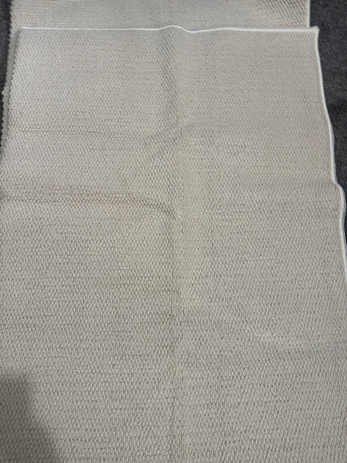 Close-up of a neutral grey-beige textured rug with bound edges